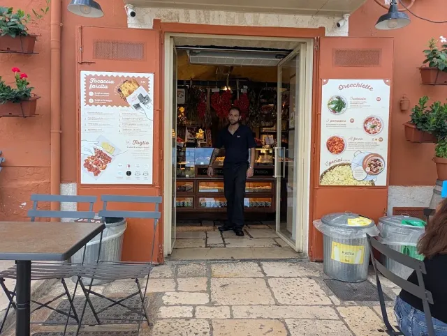 חזית כתומה עם פתח פתוח ואיש עומד בו, כרזות תפריט ושולחנות בחוץ