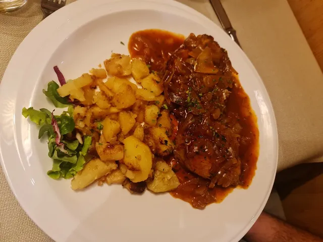 נתח בשר ברוטב עשיר לצד תפוחי אדמה צלויים וסלט ירוק בצלחת לבנה