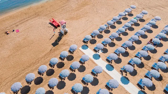 מבט מלמעלה על שורות שמשיות מפוספסות כחול לבן על חול זהוב