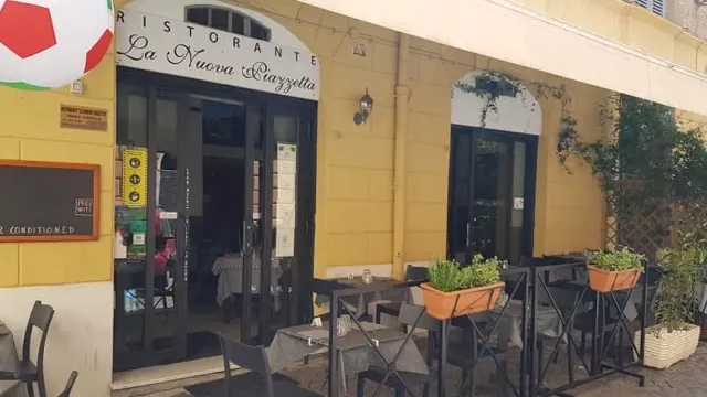 פינת מבנה צהוב עם דלתות כהות, שולחנות בחוץ ואדניות עשבי תיבול