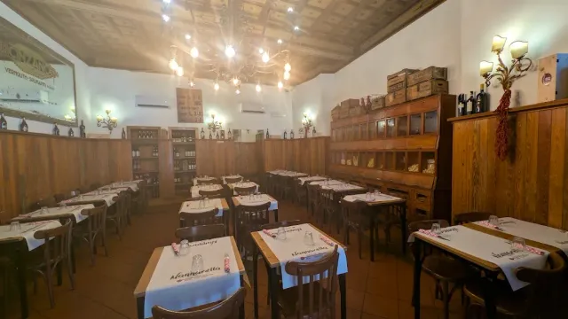 אולם ריק עם חיפוי עץ, נברשת נורות ושולחנות במפות לבנות ואדומות
