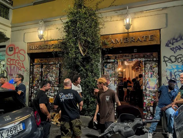 אנשים עומדים בערב מול חזית מכוסה מדבקות וצמח מטפס, עם פנסים דולקים