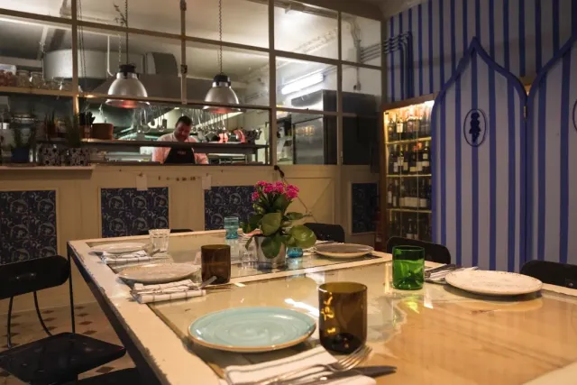 שולחן ארוך ערוך בצלחות וכוסות צבעוניות מול מטבח פתוח וקיר פסים