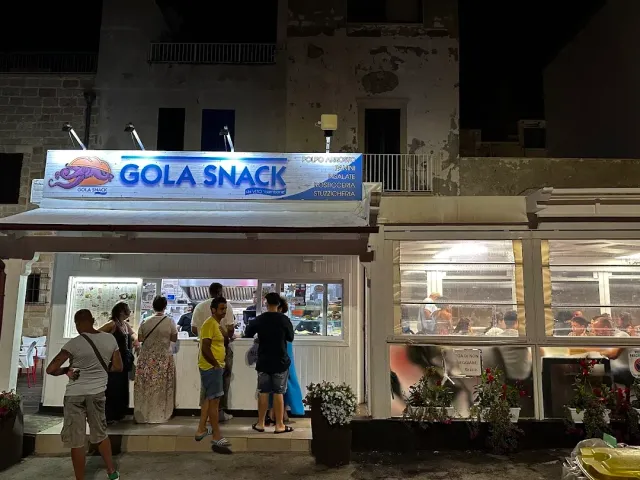 דוכן מואר בלילה עם שלט כחול, אנשים ממתינים בתור מול הדלפק
