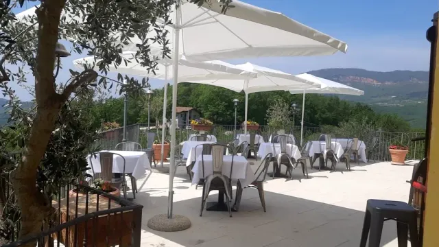מרפסת רחבה עם שמשיות לבנות ושולחנות ערוכים, גבעות ירוקות באופק
