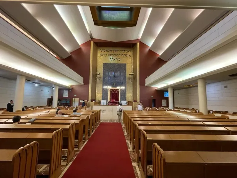 אולם תפילה עם ספסלי עץ בשתי שורות, שביל שטיח אדום וארון קודש בקצה
