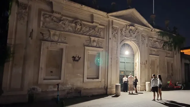 שער אבן מעוטר בתבליטים, מואר בלילה, ולידו כמה אנשים עומדים