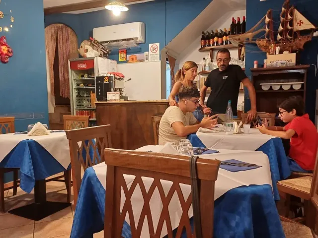 חדר בקירות כחולים עם סועדים לשולחן, מפות כחול לבן ודגם ספינה במדף