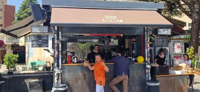 דוכן מתכת עם סוכך וכמה אנשים מזמינים בדלפק החיצוני, בין עצים