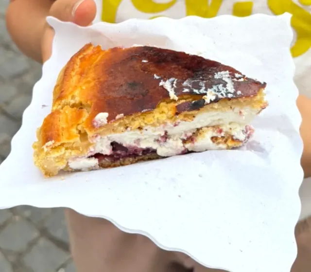יד מחזיקה על נייר פרוסת עוגה שרופה מעט במילוי גבינה ודובדבנים