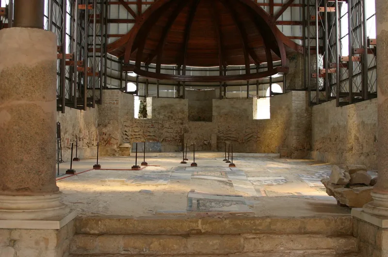 אולם באתר ארכיאולוגי מתחת לגג הגנה מודרני עם רצפת אבן מגוונת וקירות חשופים
