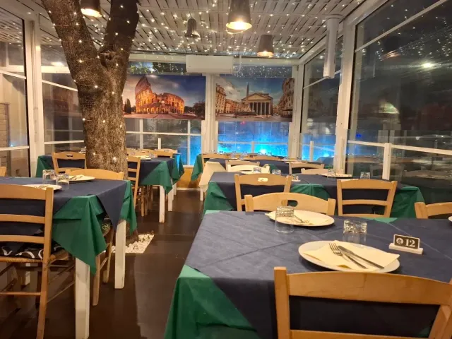 מרפסת מזוגגת עם שולחנות כחולים וירוקים, גזע עץ מקושט באורות וציור קיר