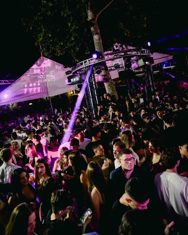 קהל צפוף רוקד בחצר פתוחה תחת אורות במה סגולים בלילה