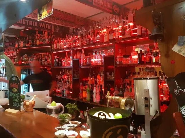 בר באור אדום עם מדפי בקבוקים צפופים, לוח גיר ודלי קרח על הדלפק