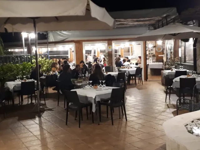 רחבת חוץ בלילה עם שמשיות, מפות לבנות וסועדים סביב השולחנות