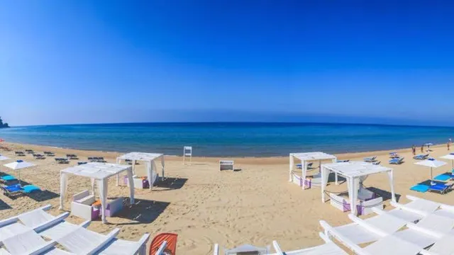 סוכות לבנות ומיטות שיזוף על חוף חולי רחב מול ים כחול