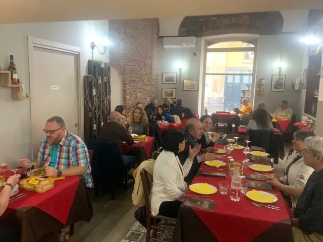 סועדים לאורך שולחנות במפות אדומות וצלחות צהובות, קיר לבנים חשוף מאחור