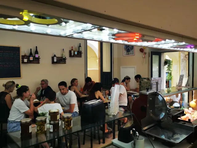 סועדים צפופים סביב שולחנות, פורסת נקניק וצנצנות זיתים על הדלפק